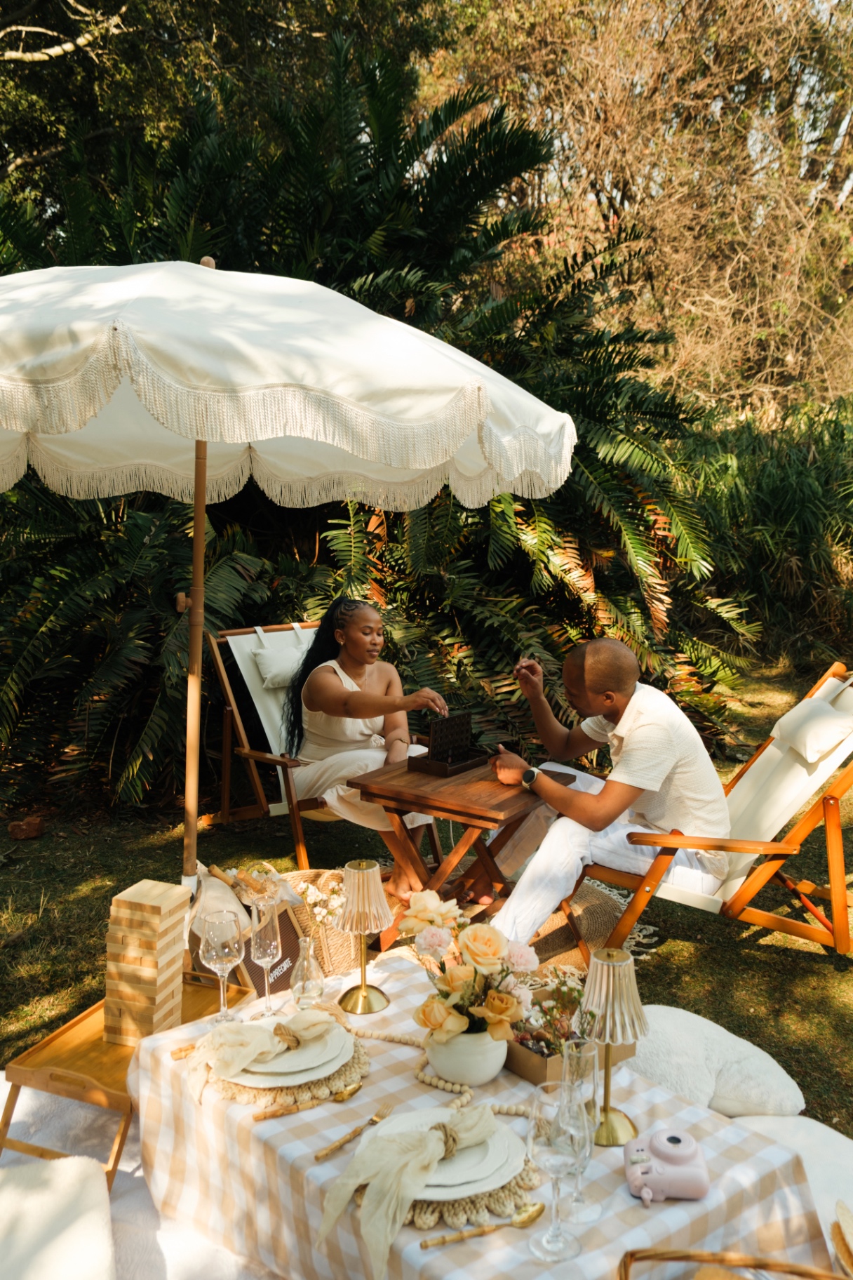 Gingham picnic tablescape for two under a fringed umbrella